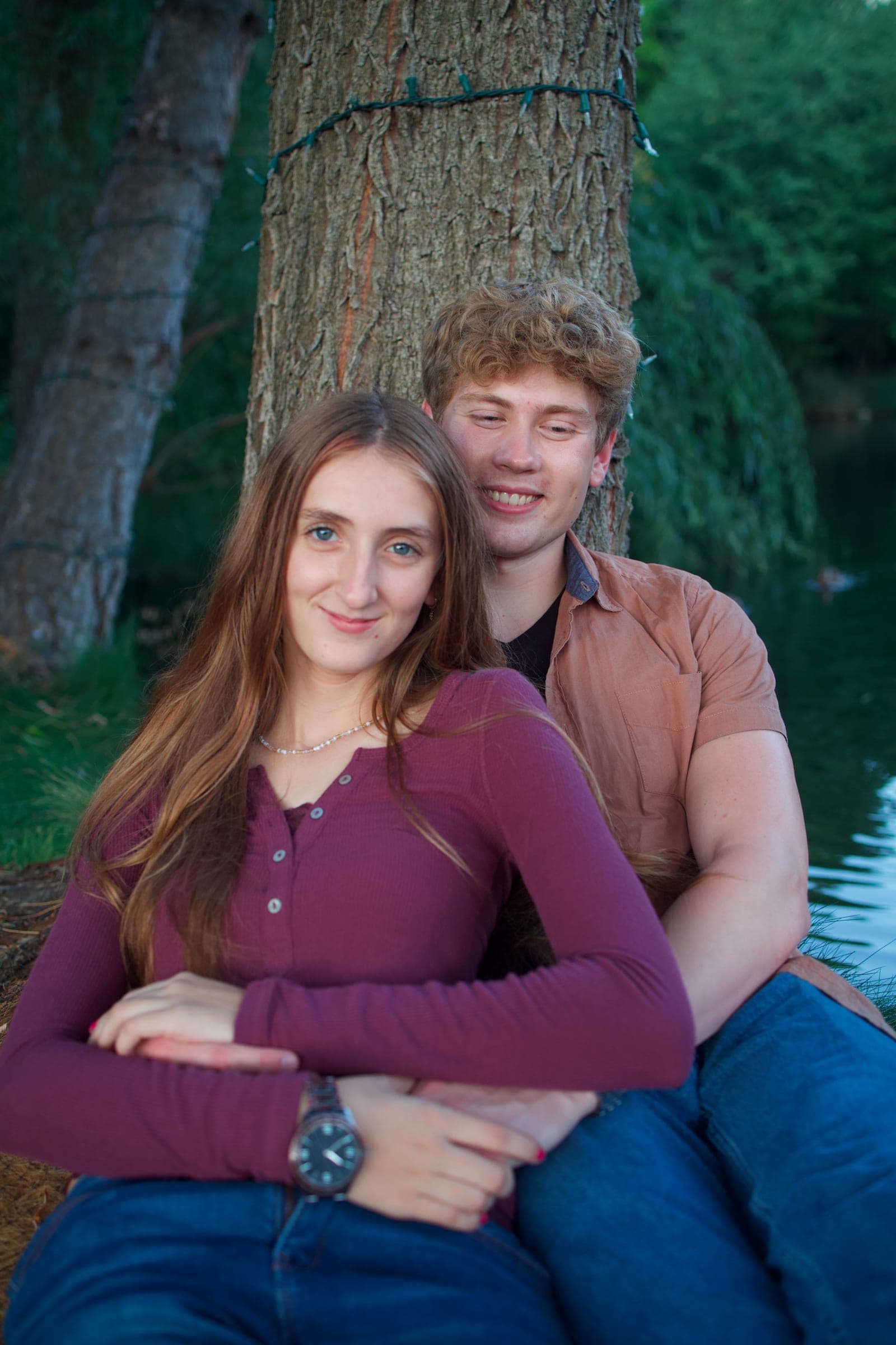 Molly and Tyler sitting together against a tree by the water